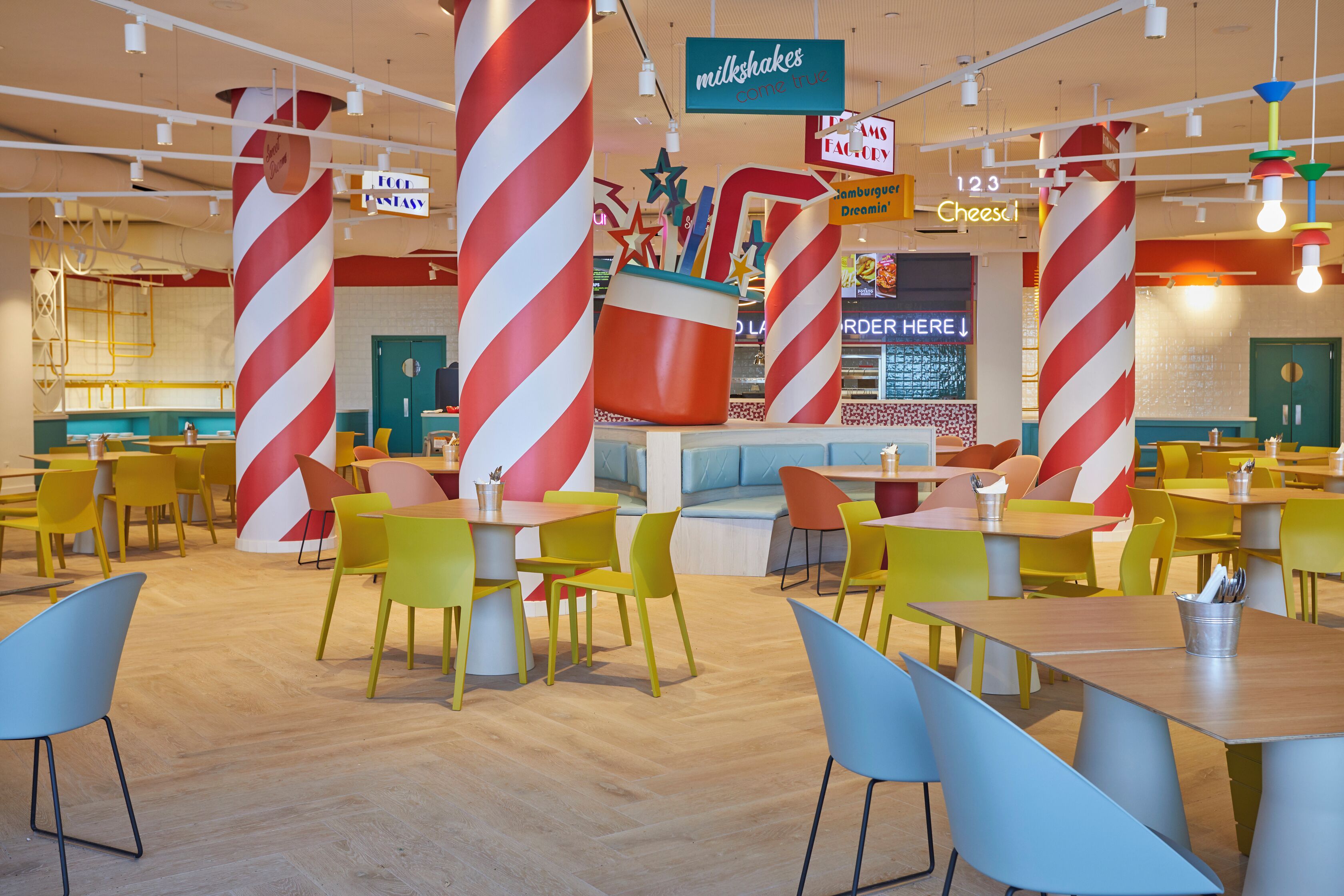 Un restaurante muy iluminado con sillas y mesas de colores, un gran pilar con forma de bastón de caramelo y un letrero de batidos.