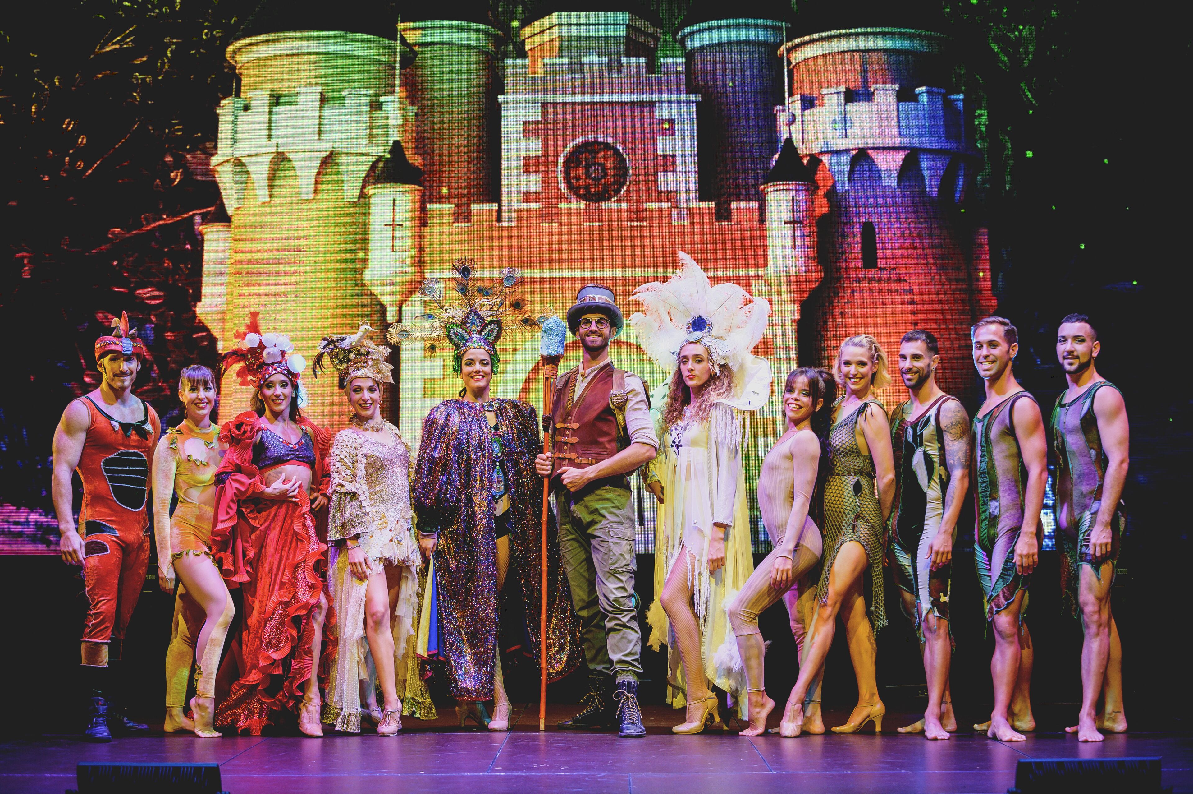 A group of people in costumes standing in front of a castle backdrop.