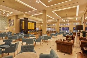 Un hall d’entrée spacieux avec plusieurs coins salon, un bar et une grande fenêtre offrant une vue sur la ville.