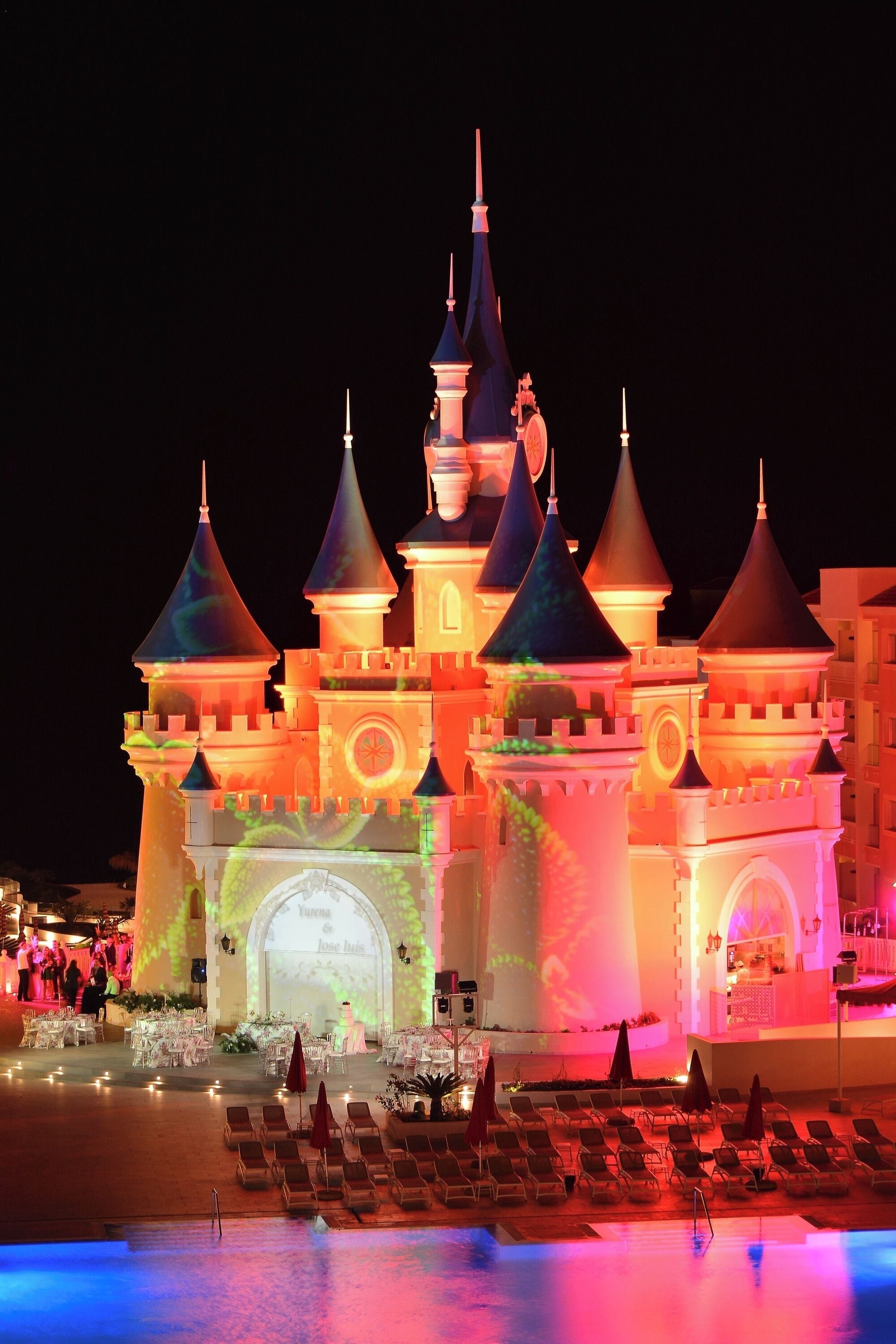A castle-like hotel with multiple towers, a pool area with lounge chairs, and a reception area.