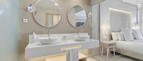 A modern bathroom with two sinks, a bench, and a bedside table.
