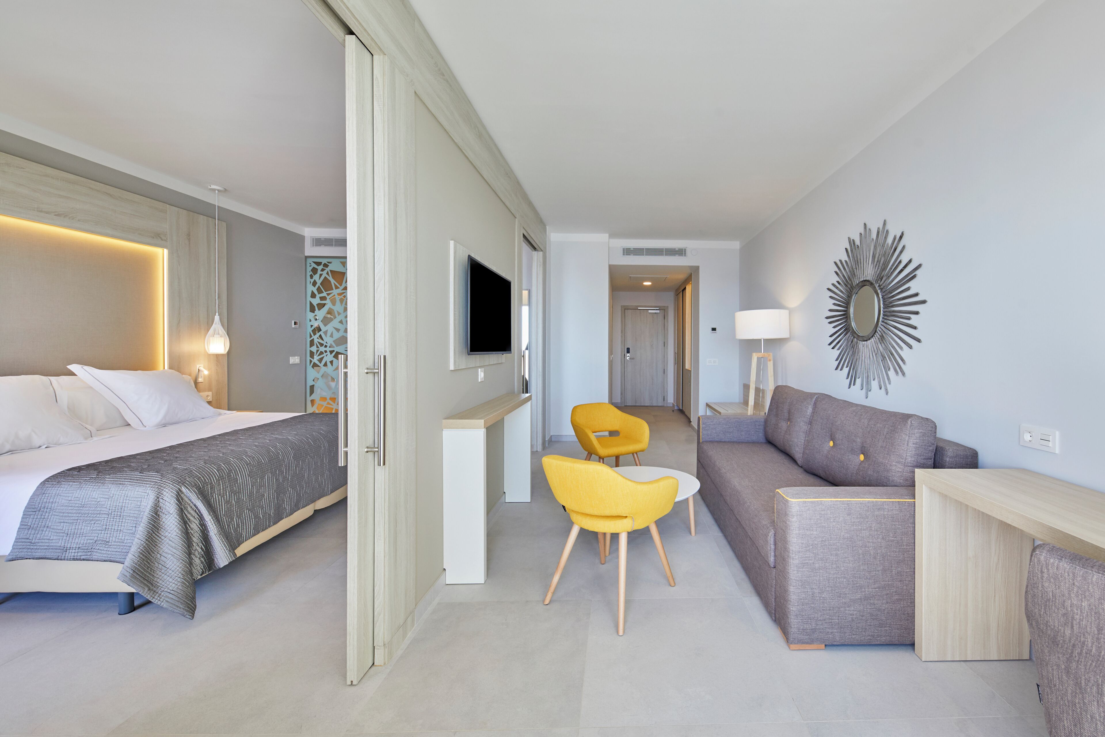 A modern hotel room with a bed, a sofa, a desk, and two chairs.