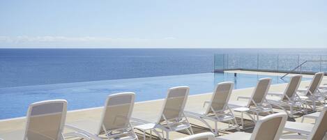A poolside area with lounge chairs facing the ocean.