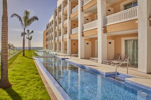 Une piscine située à côté d’un hôtel doté de nombreux balcons, d’une pelouse et de palmiers.