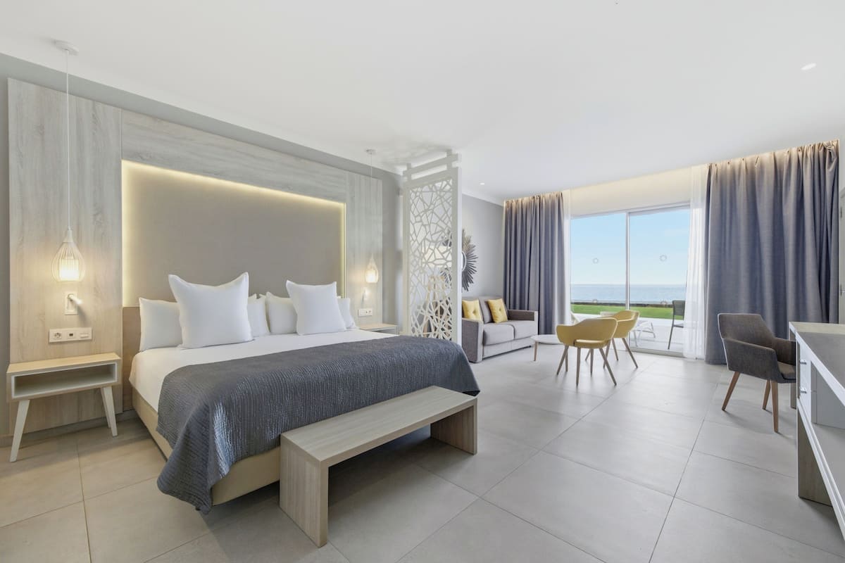 Une chambre moderne avec un grand lit, des tables de chevet, un banc, un canapé et un coin repas avec des chaises.
