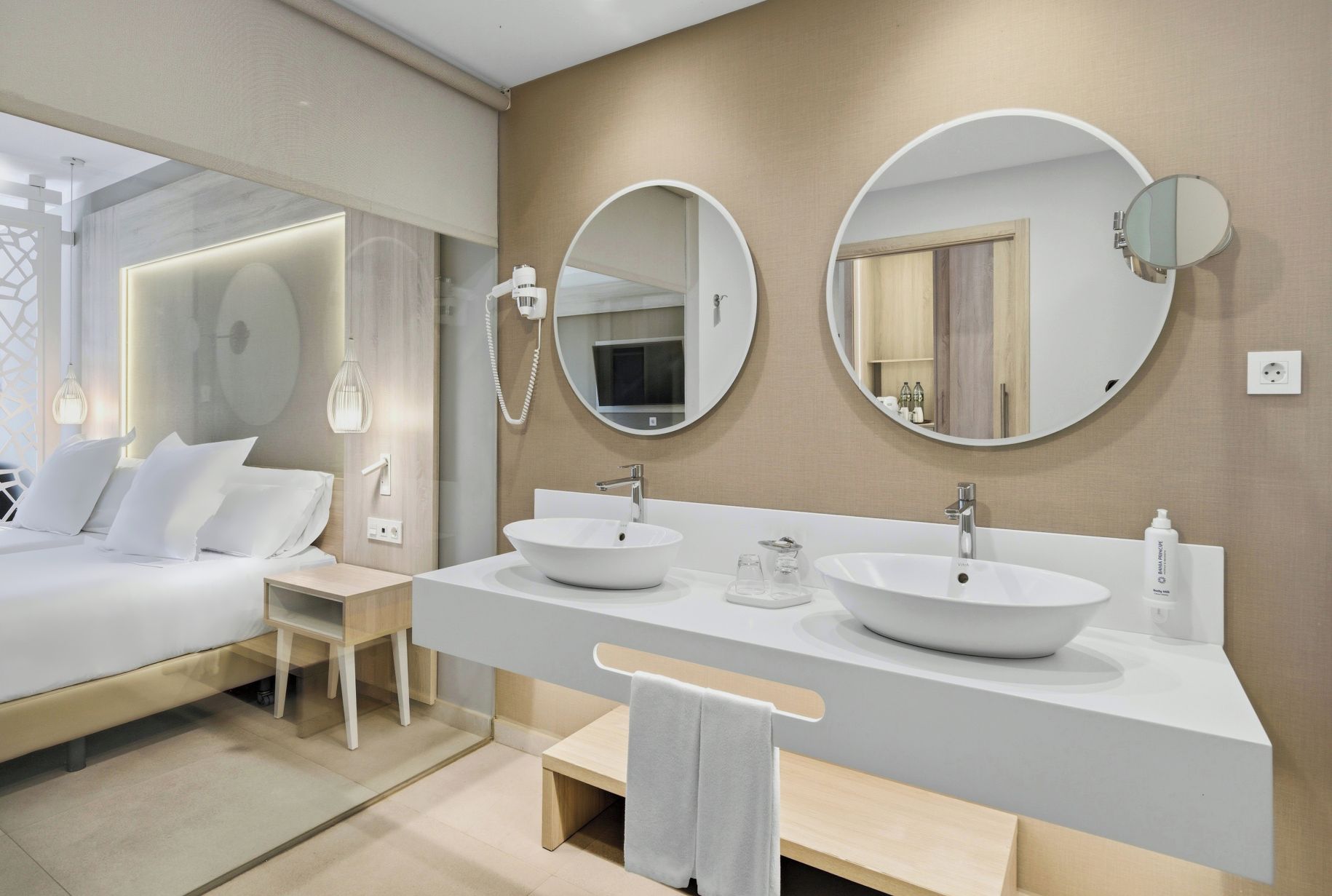 Een moderne hotelbadkamer met twee wastafels, een spiegel en een nachtkastje.