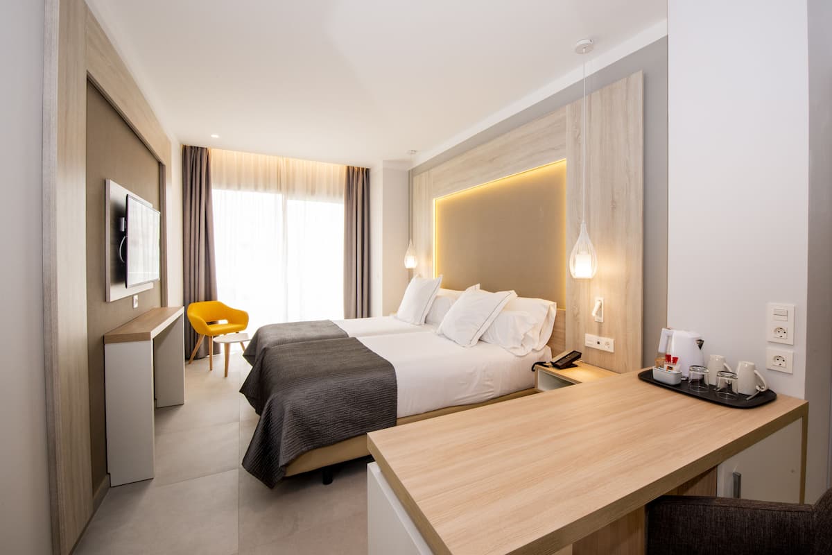 Une chambre d’hôtel avec un lit, une table de chevet, un bureau, une chaise et un téléviseur fixé au mur.