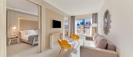 Moderni hotellihuone, jossa on sänky, televisio, sohva ja ruokailutila tuoleineen.