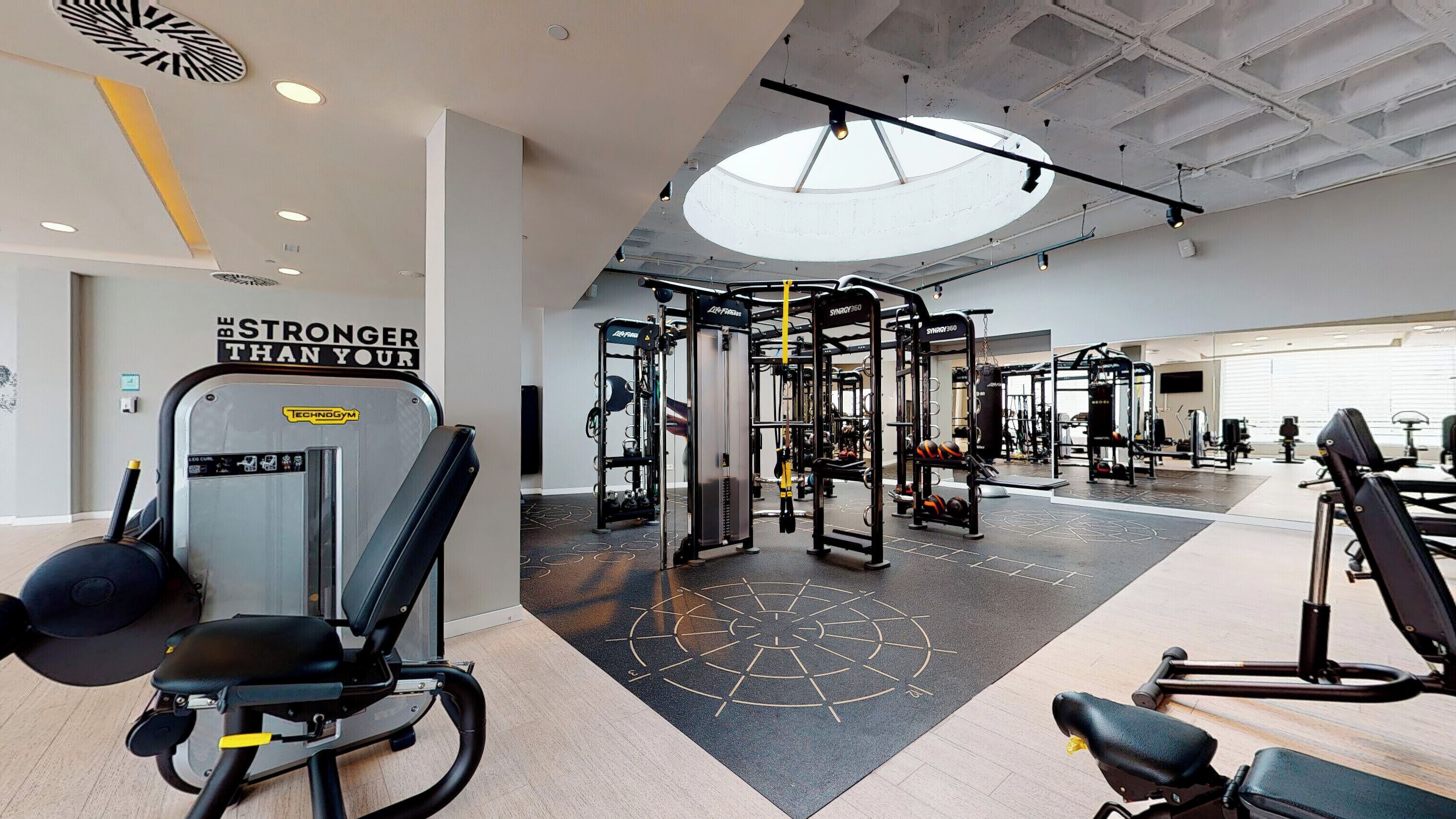 A gym with various exercise machines, a motivational wall, and a skylight.