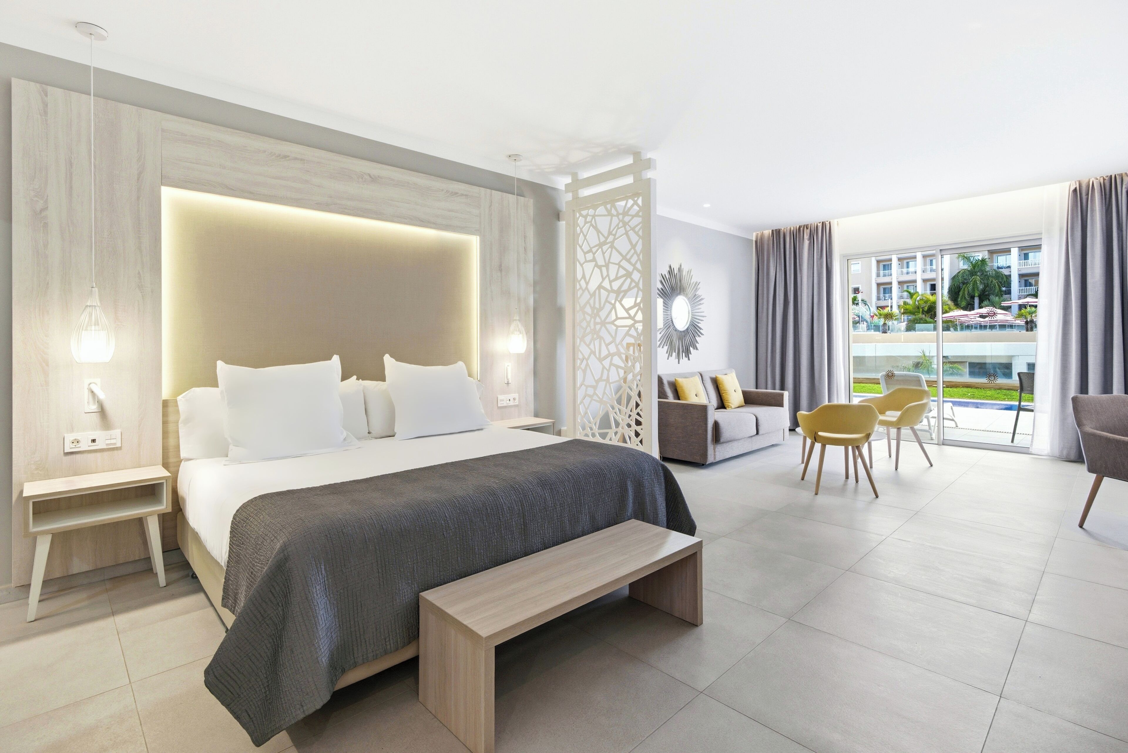 Ein modernes Hotelzimmer mit einem großen Bett, einer Bank, einer Couch und einem Essbereich mit Stühlen.