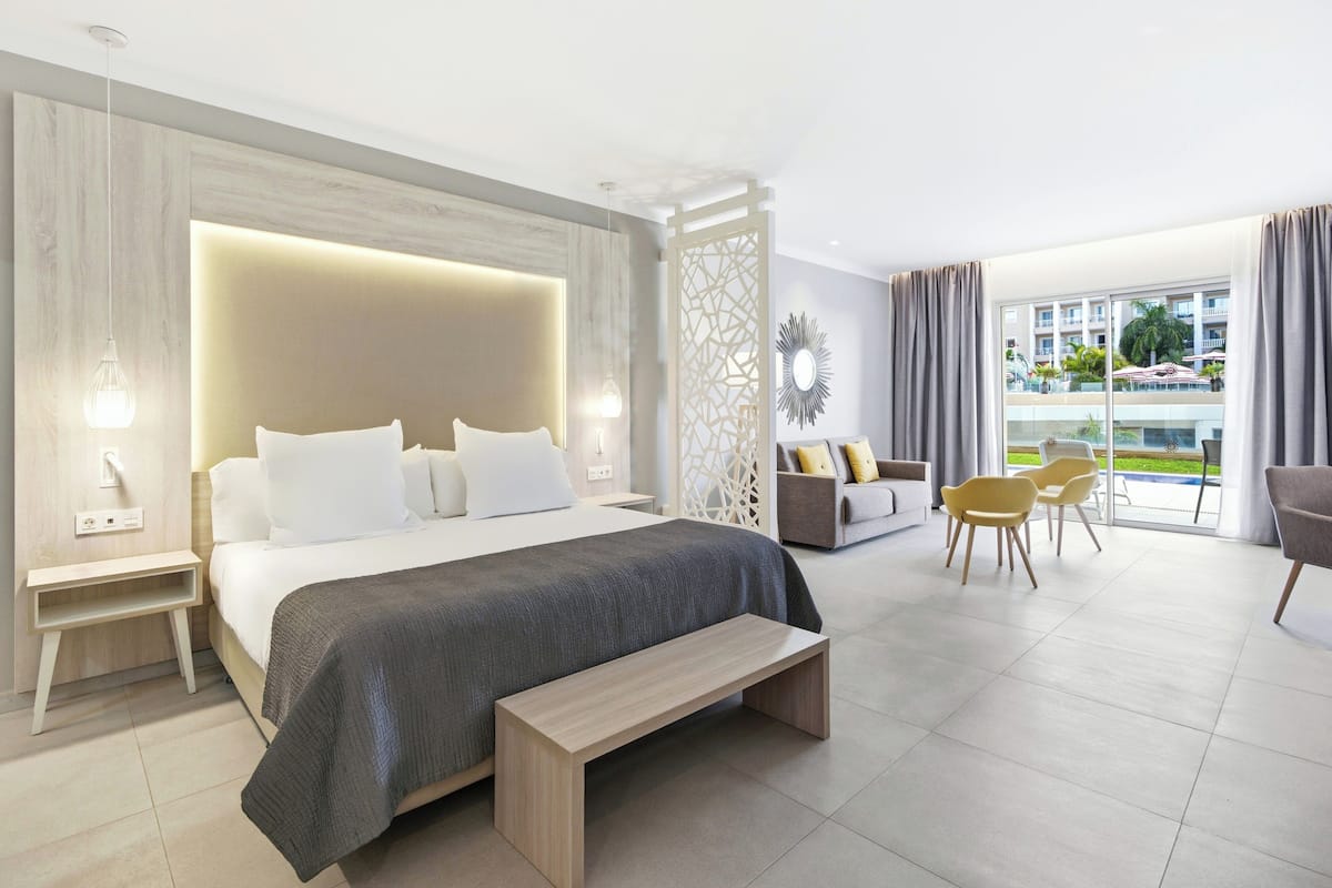 Une chambre d’hôtel moderne avec un grand lit, une banquette, un canapé et un coin repas avec des chaises.