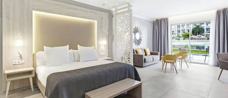 A modern hotel room with a large bed, a bench, a sofa, and a dining area with chairs.
