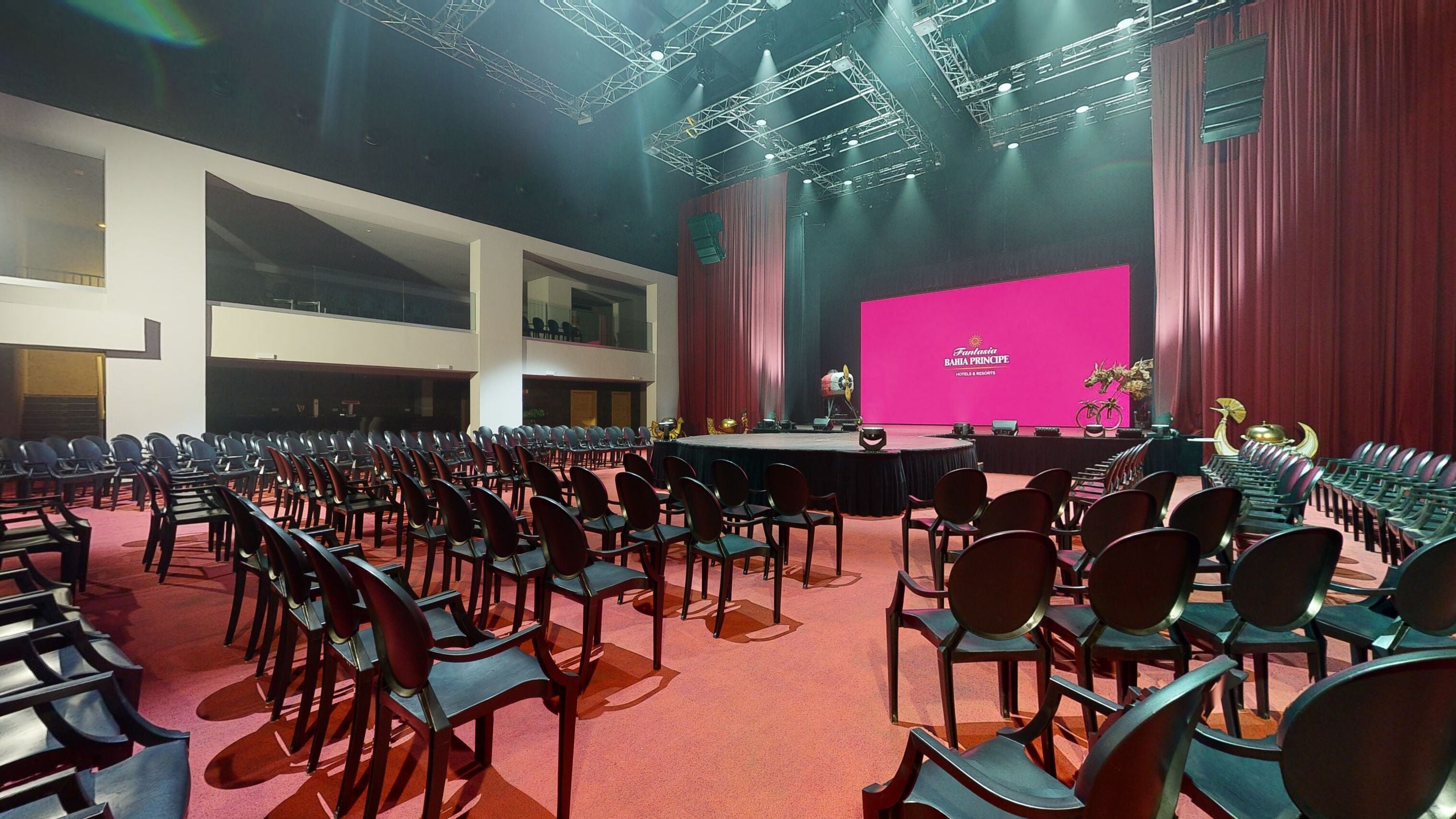 A conference room with rows of chairs, a stage with a pink backdrop, and a large screen displaying 'Fantasca Bahia Principe Hotels & Resorts'.