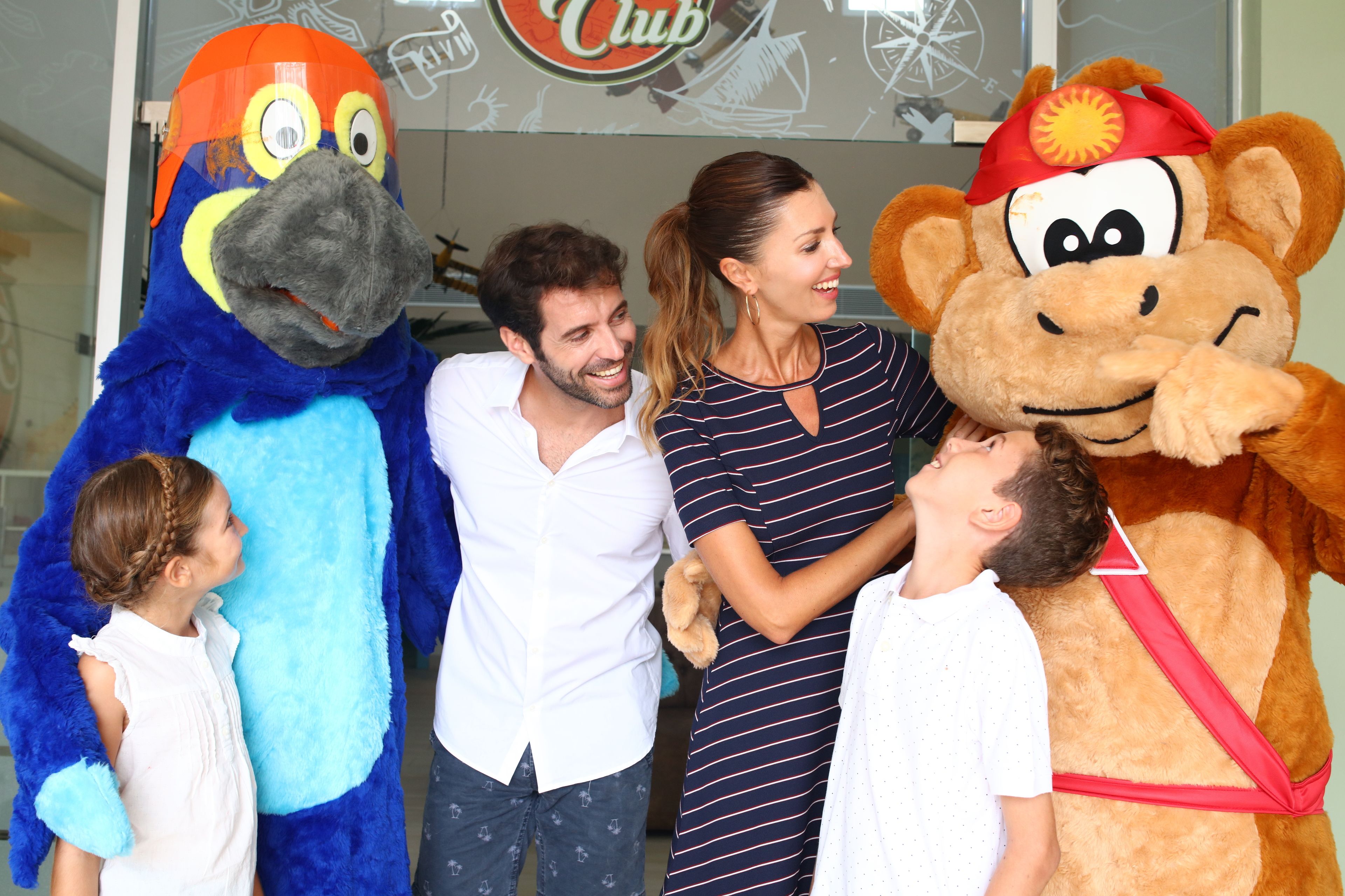 A group of people with two mascots, one blue and one brown, in front of a sign with the word "Club".