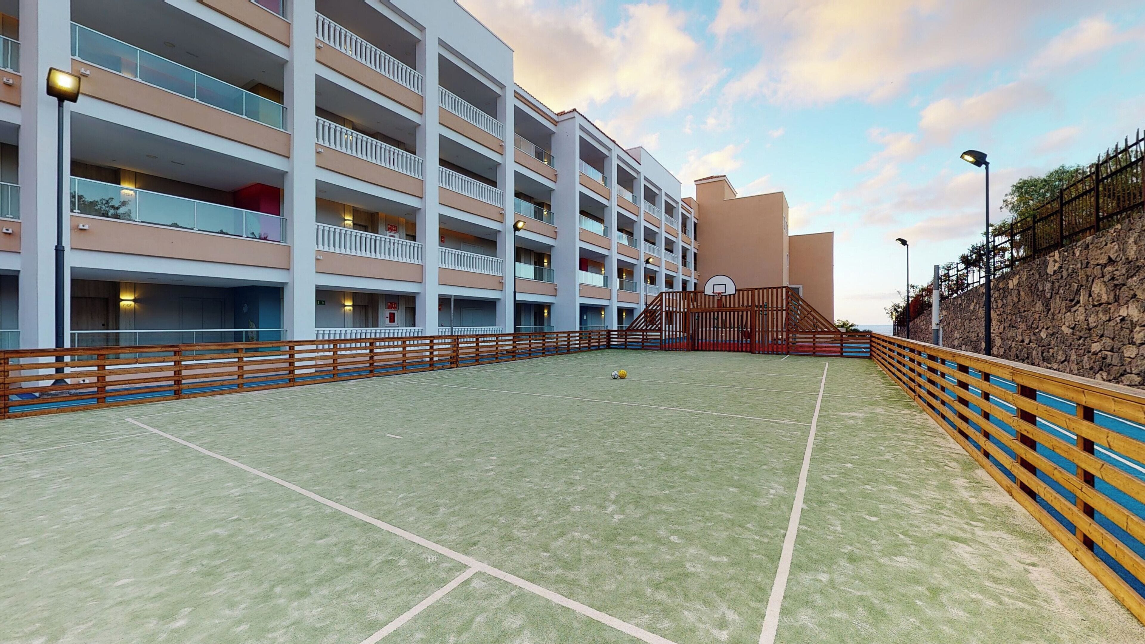 A multi-story hotel with balconies, a basketball court, and a stone retaining wall.
