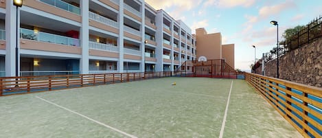 A multi-story hotel with balconies, a basketball court, and a stone retaining wall.