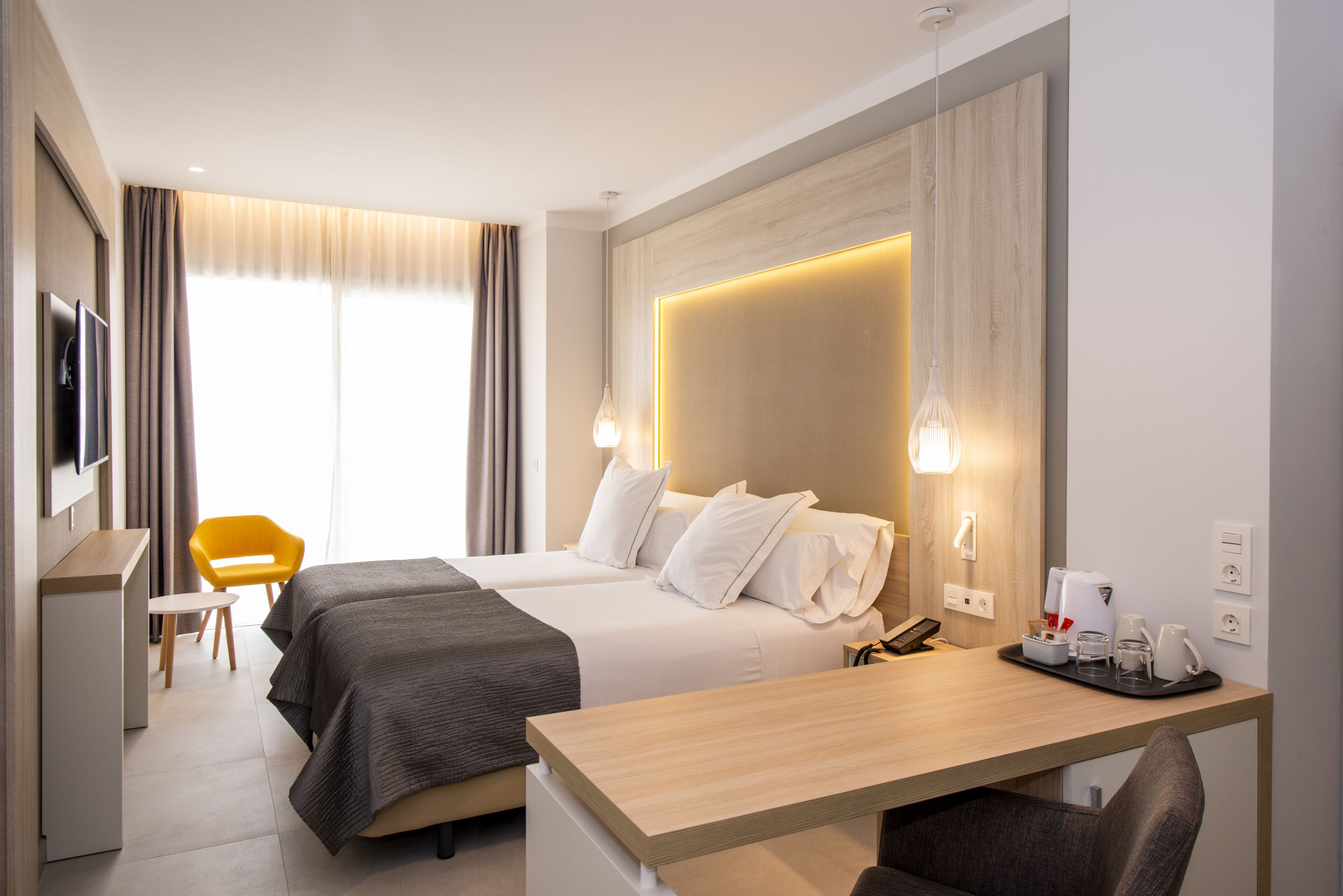 A modern hotel room with two beds, a desk, a chair, a TV, and a window with curtains.