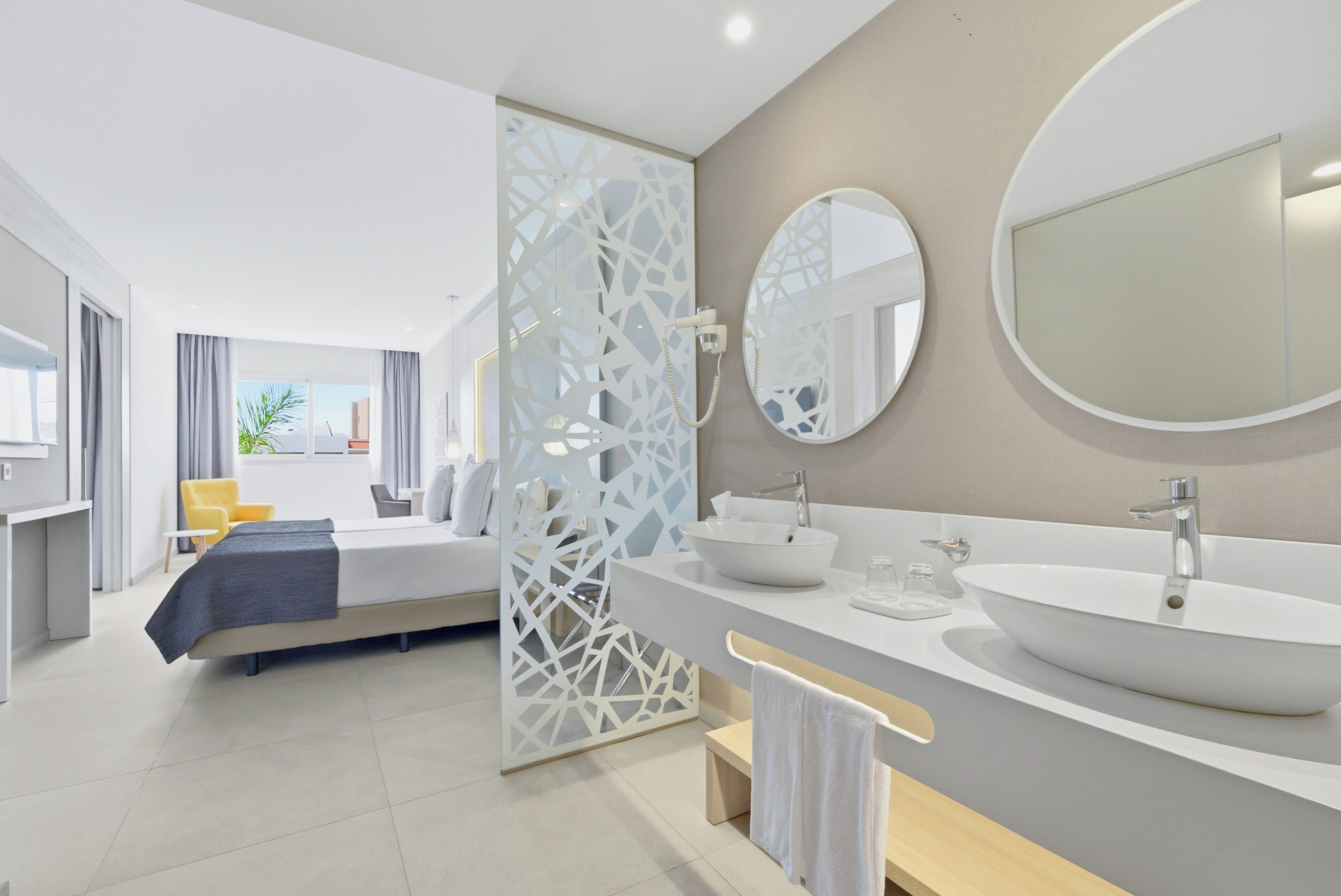 Un baño de hotel moderno con un lavamanos grande, dos espejos y una zona de ducha.