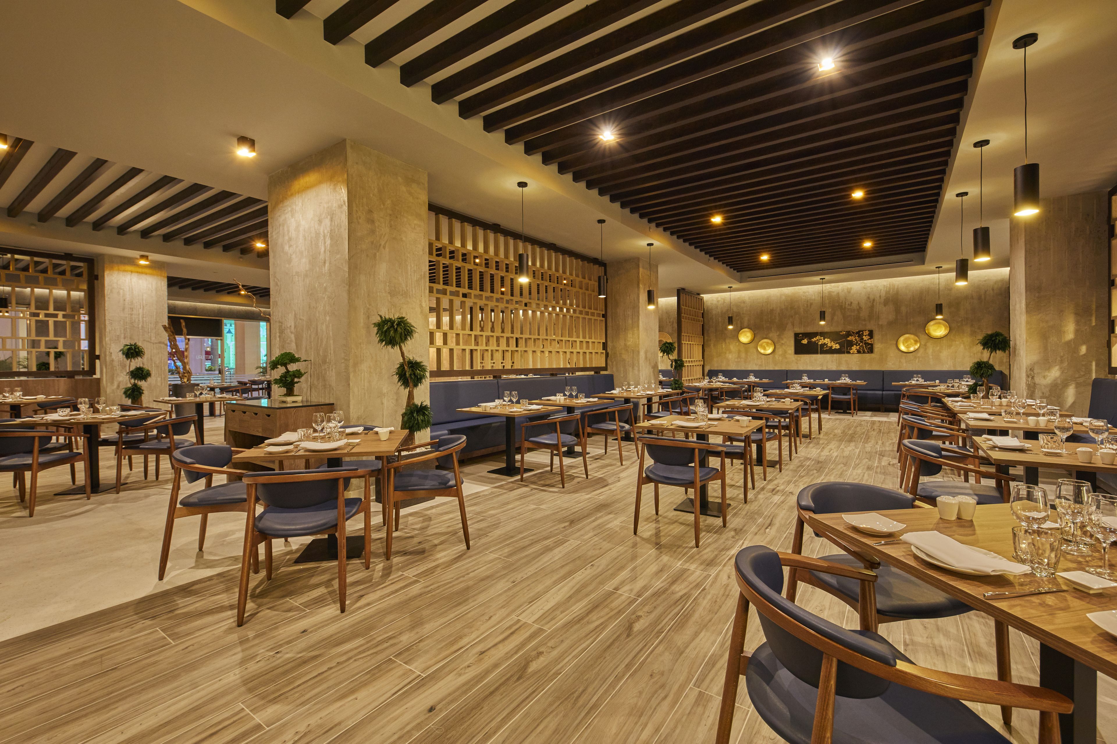 Un restaurant spacieux doté d’un plancher en bois, de nombreuses tables et chaises, et d’un design moderne au niveau du plafond.