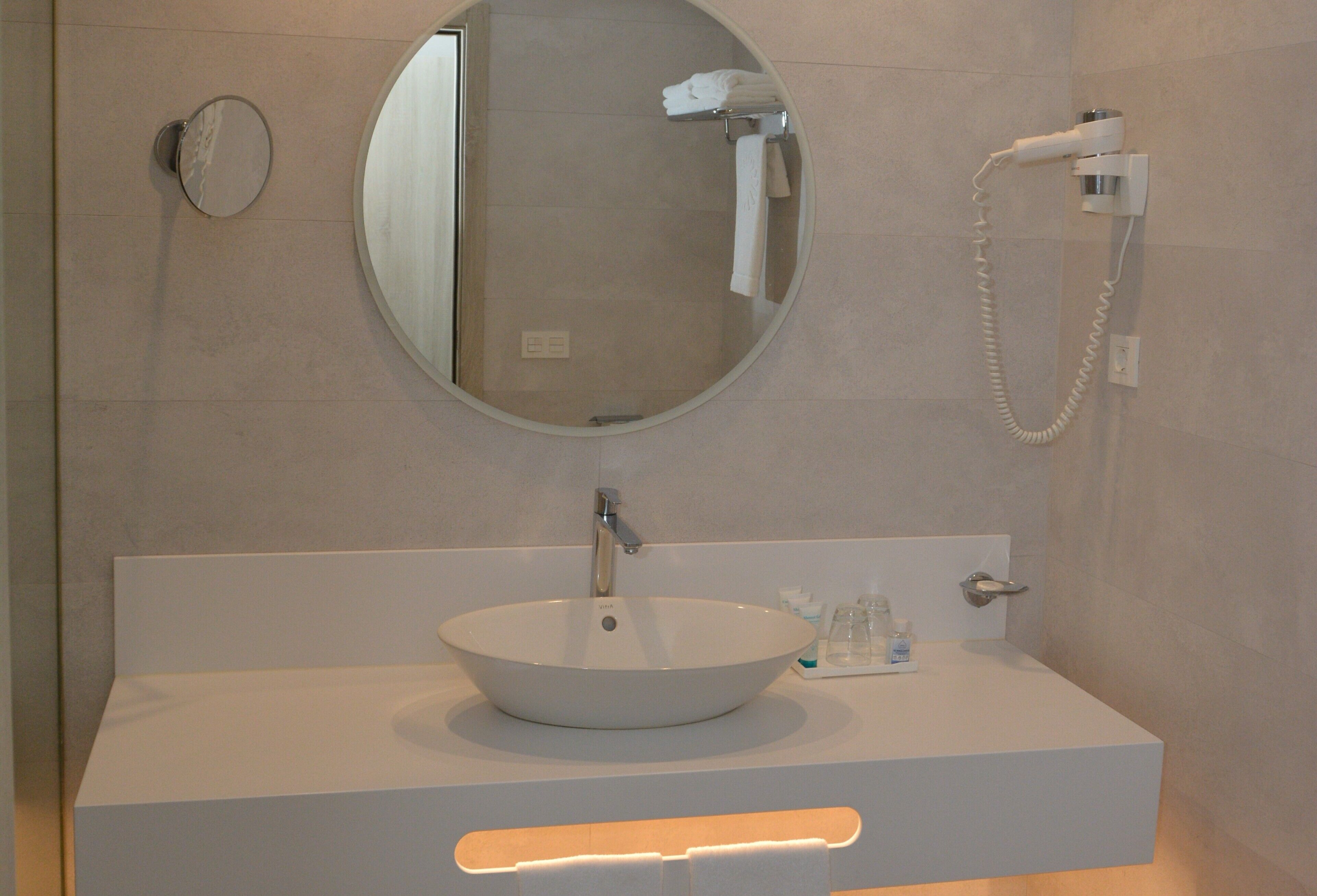 A bathroom with a round mirror, a white sink, and a towel rack.