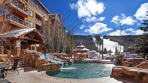 A resort pool with a water slide, lounge chairs, and a wooden building with balconies. - Modern Ground Floor Unit/1 Minute Walk to the Gondola/Great Amenities (Keystone)