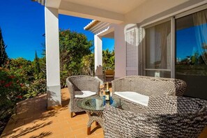 Relax in the serene outdoor seating area with a wicker sofa and chairs, surrounded by lush greenery and a beautiful view.