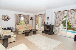 Relax in this inviting living room with a fireplace, comfortable sofa, and large windows offering a view of the pool.