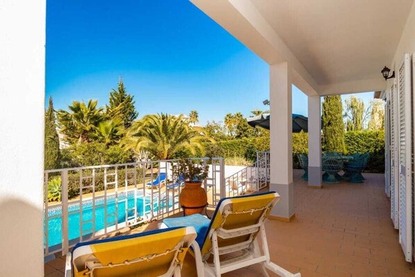 Relax on the balcony with a view of the pool surrounded by lush greenery.