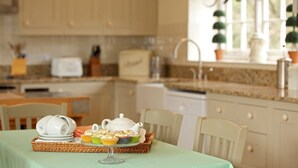 A kitchen with a dining table set for a meal, featuring a teapot, cups, and a tray of cupcakes.