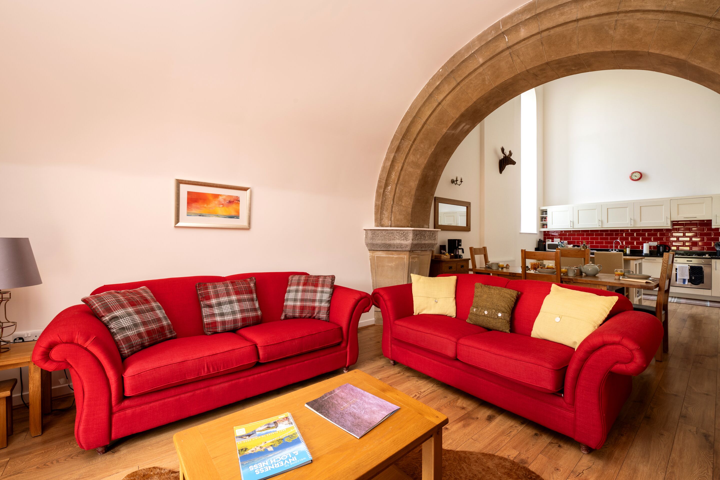 A living room with two red sofas, a wooden coffee table, and a painting on the wall.