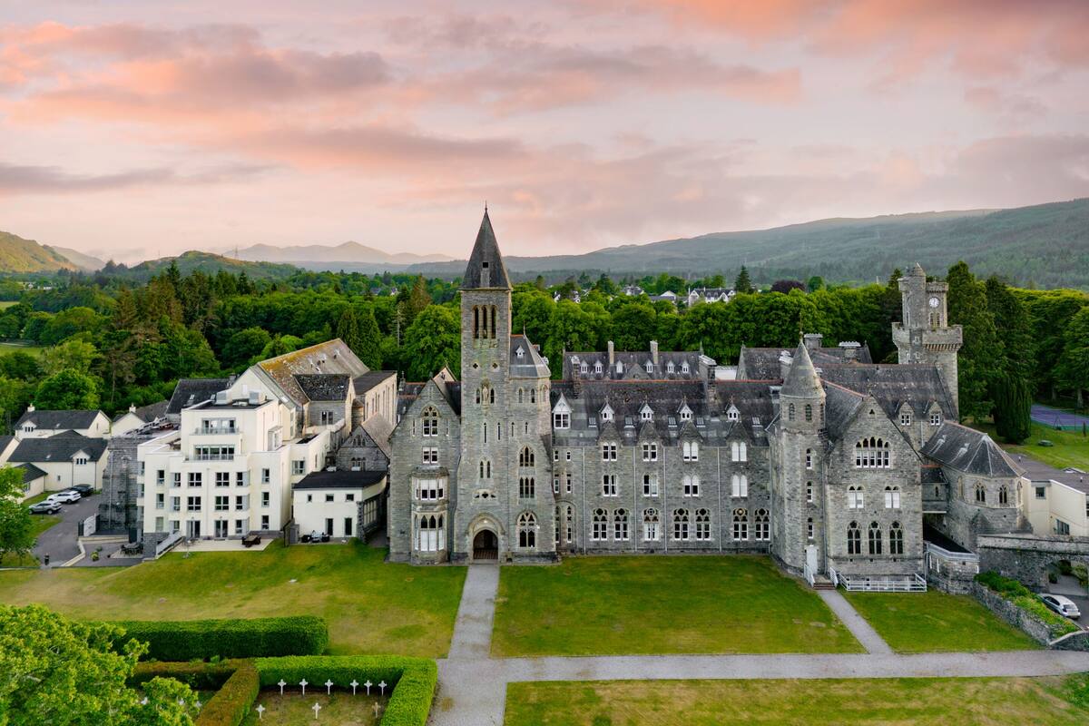 A large, historic building with a prominent tower, surrounded by lush greenery and a well-maintained lawn.