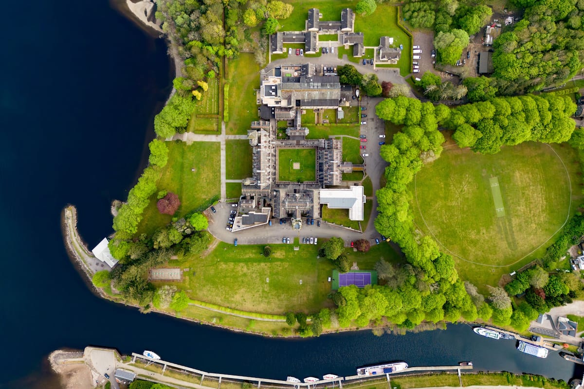 An aerial view of a coastal property with a large estate, multiple buildings, and a marina with boats.