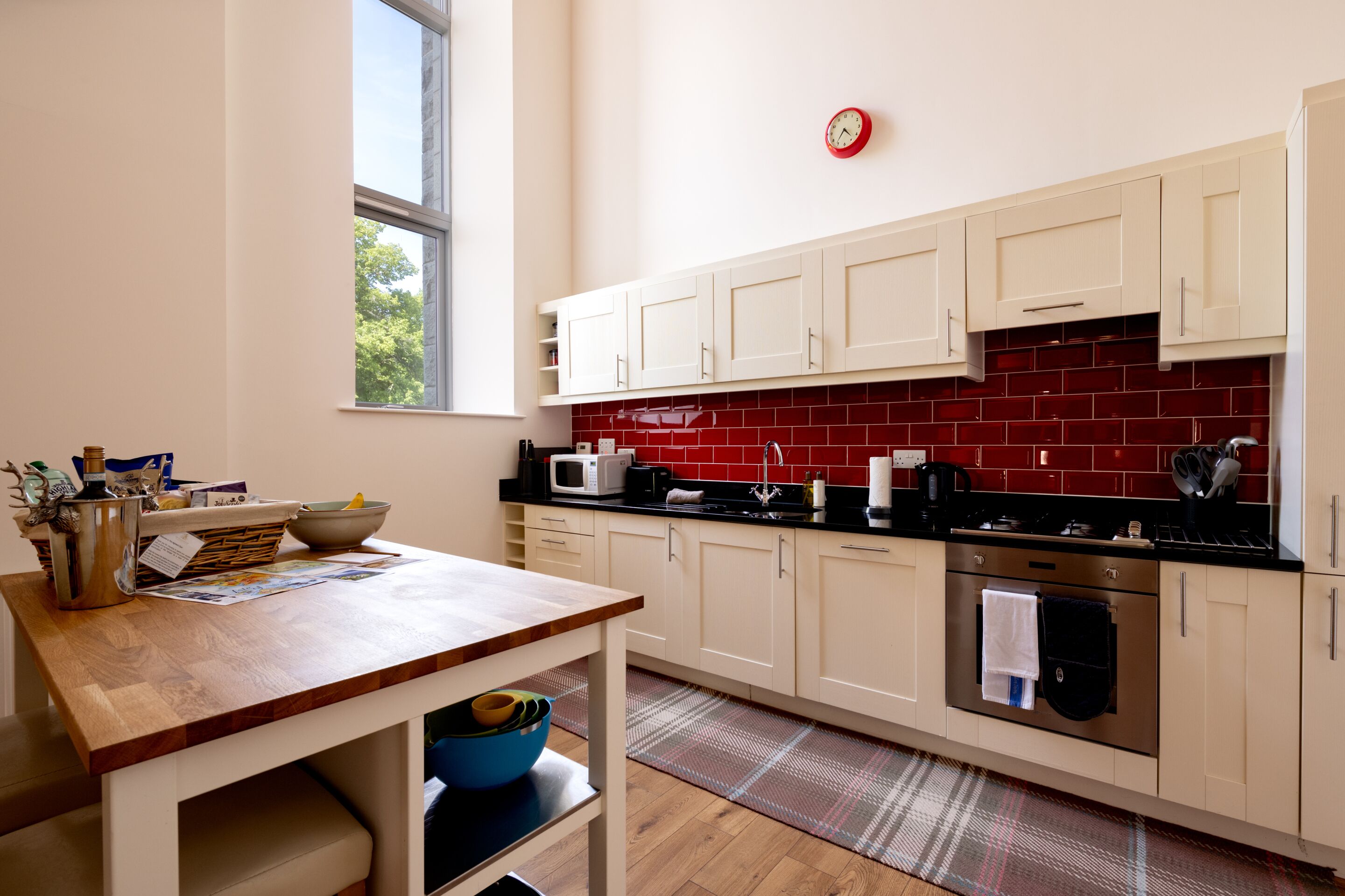 A kitchen with white cabinets, a red tiled backsplash, and a window providing natural light.