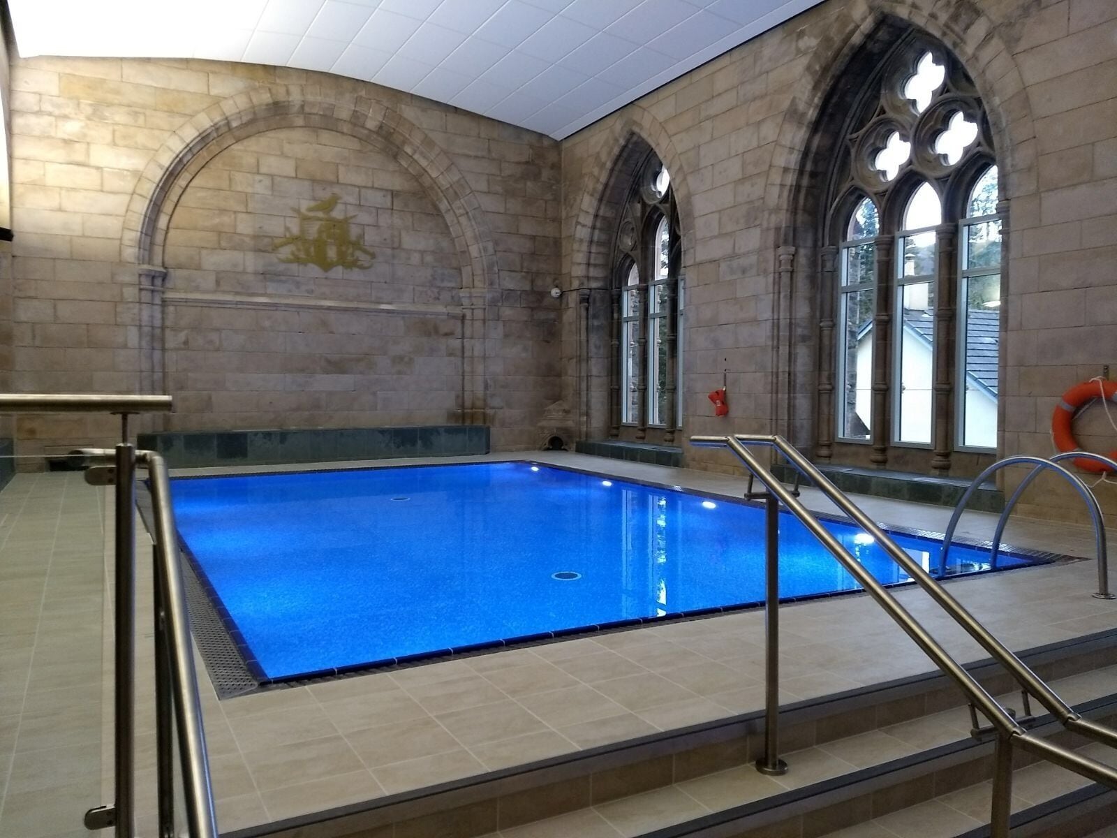 An indoor swimming pool with stone walls and arched windows.