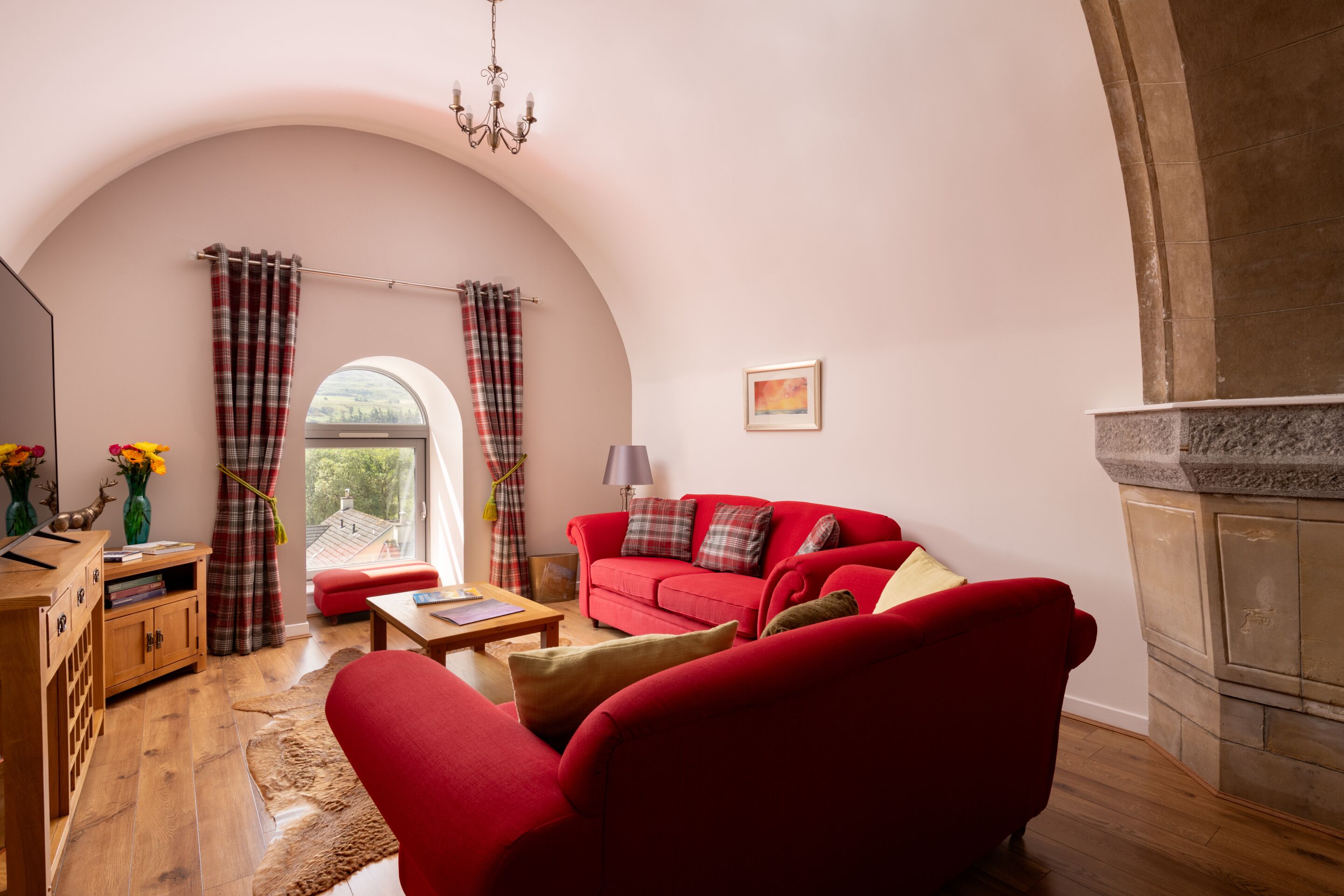 A cozy living room with a red sofa, wooden furniture, and a fireplace.