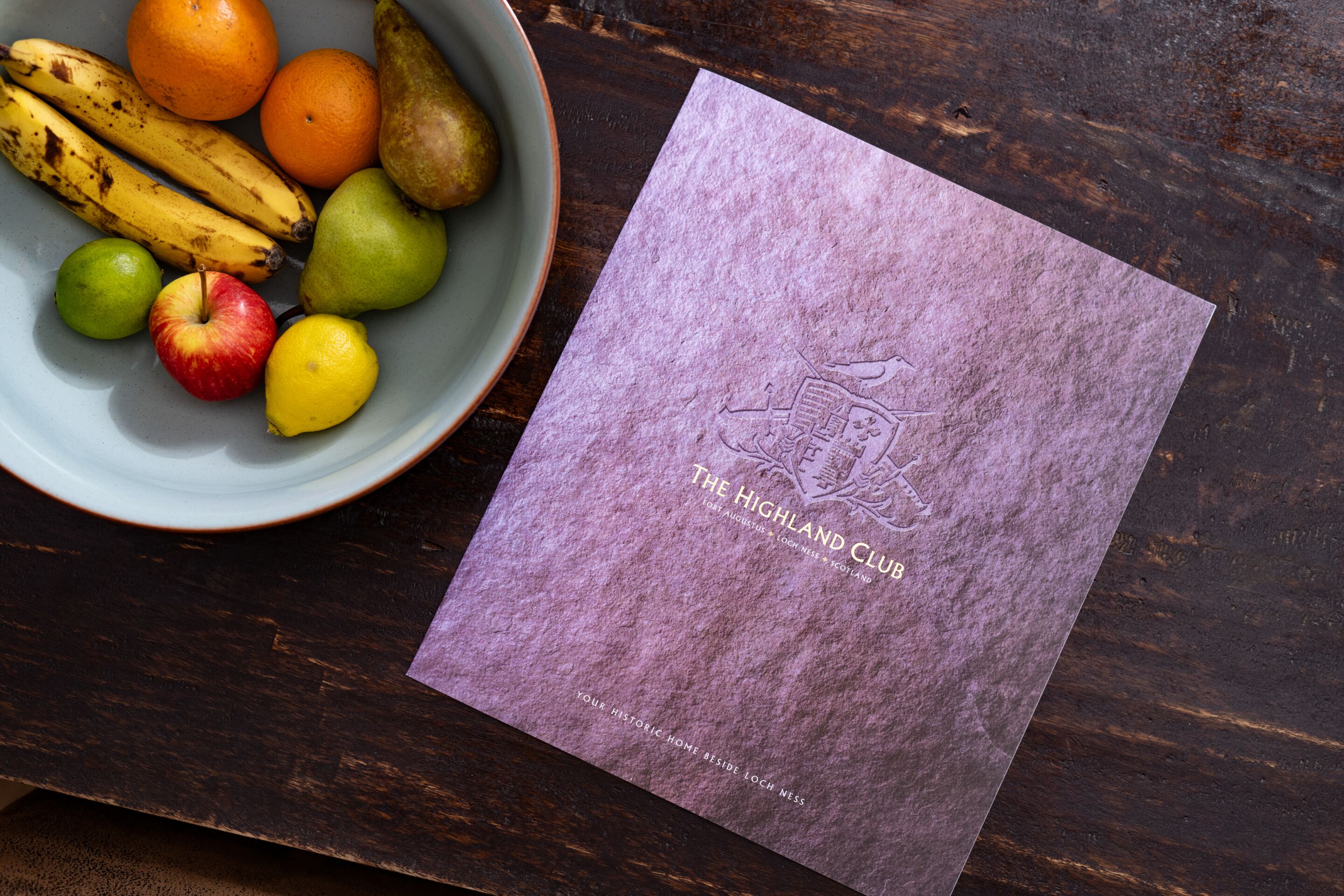 A bowl of fruit and a brochure on a wooden table.