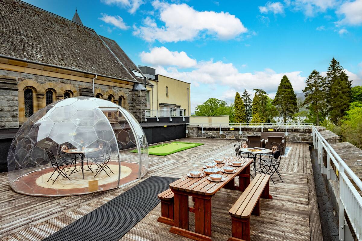A rooftop patio with a transparent dome seating area, wooden tables, and benches.