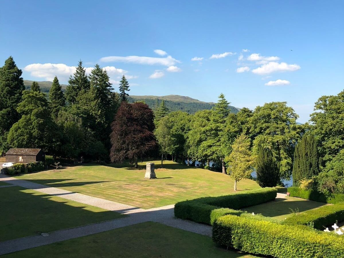 A well-maintained garden with a stone monument, neatly trimmed hedges, and a variety of trees.