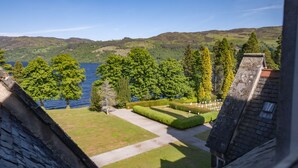 A view of a landscaped garden with a lake, trees, and a building with a sloped roof. - The Highland Club (Fort Augustus)