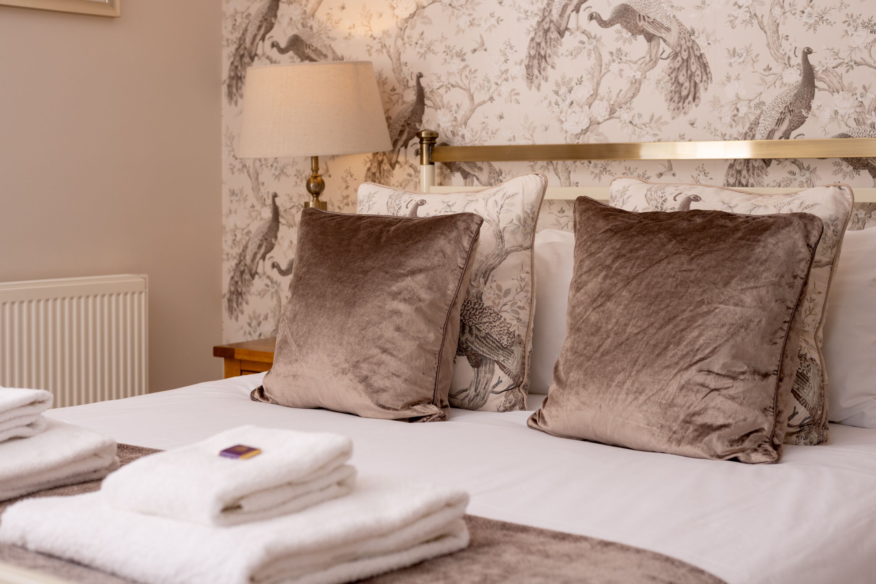 A neatly made bed with a headboard, two pillows, and folded towels.