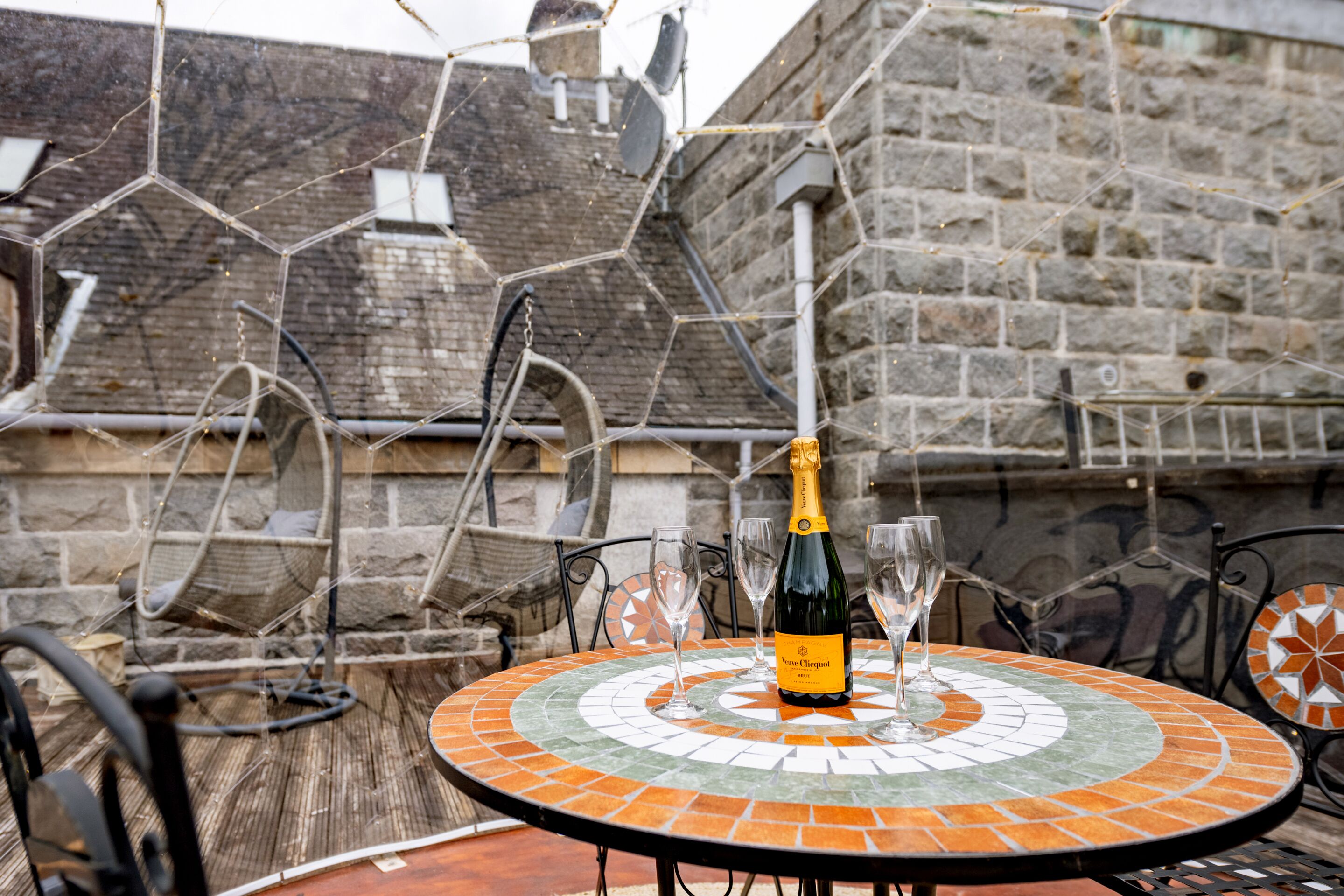 A round table with a mosaic tile design, a bottle of champagne, and two glasses on it.