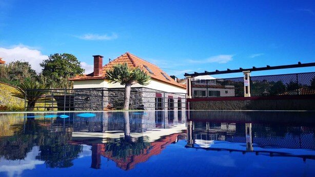 Una piscina con reflejos nítidos, un muro de piedra y un edificio con tejado de baldosas.