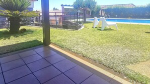 Un patio cubierto con suelo de baldosas, una palmera y vistas a una piscina y edificios a lo lejos.