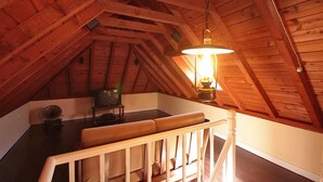 Una habitación en el ático con techo de madera inclinado, un banco de madera, una mesa con lámpara y una radio antigua.