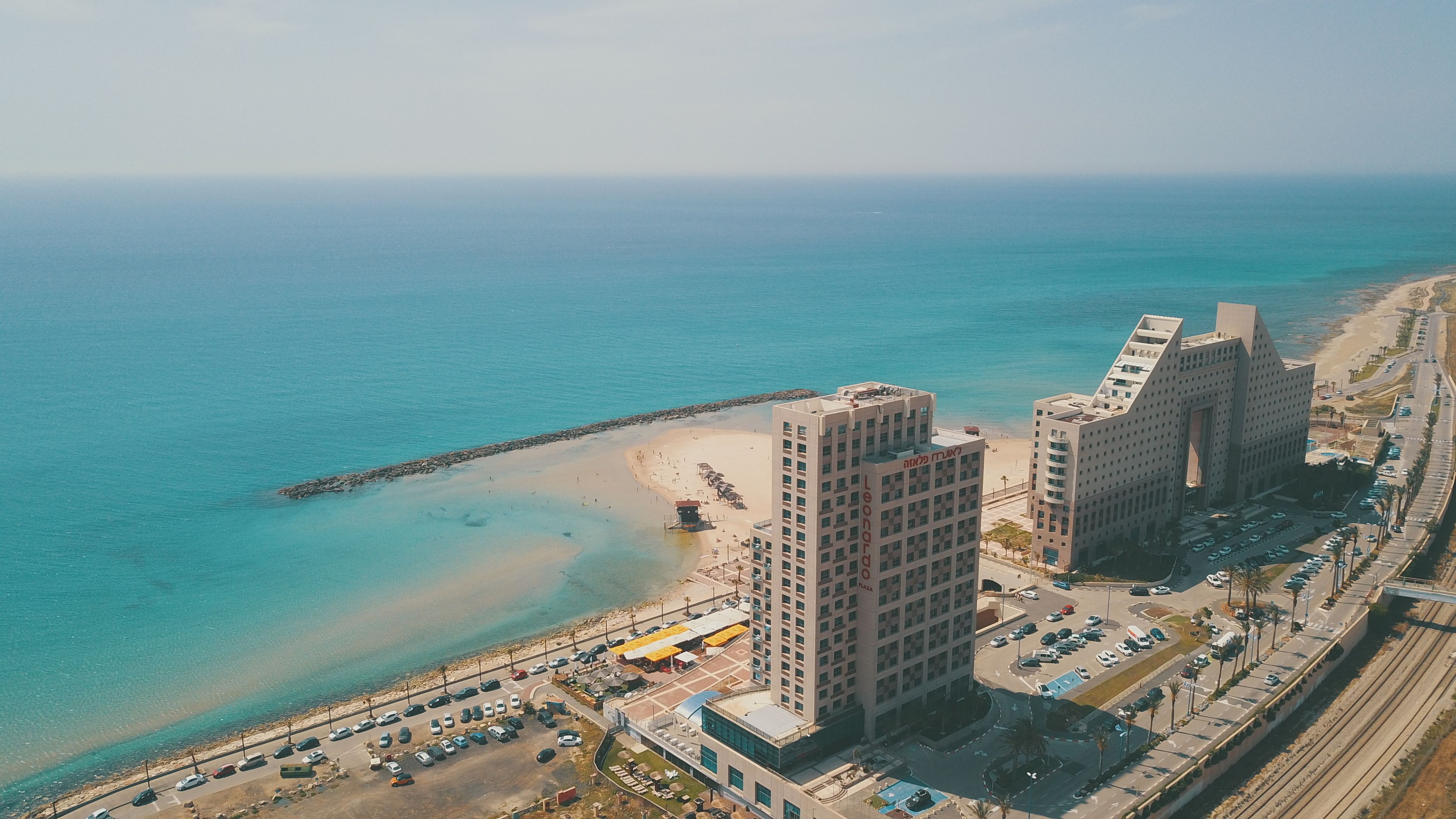 Vista aérea de uma área costeira com uma praia, um cais e dois edifícios altos de destaque.