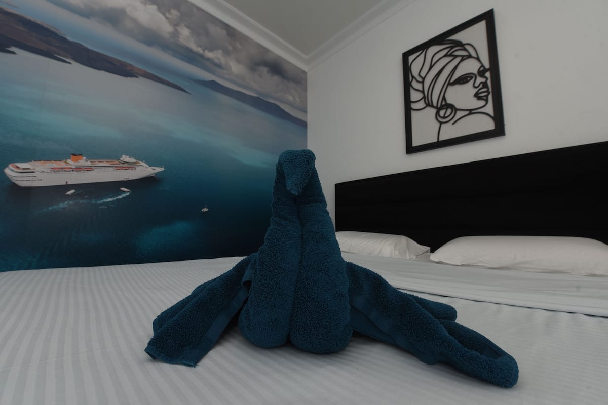 Quarto de hotel com uma cama, um mural grande de um navio de cruzeiro na parede e uma obra de arte emoldurada acima da cama.