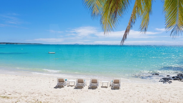 Una playa con agua turquesa cristalina, arena blanca y una fila de sillas de sol vacías.