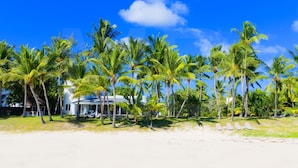 Una playa con palmeras, un edificio blanco y sillas de playa.
