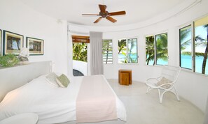 A bedroom with a bed, a ceiling fan, a chair, and large windows with a beach view. - Villa Eva - close to one of the best beaches in Mauritius, maid cooking lunch (Bellemare Plage)