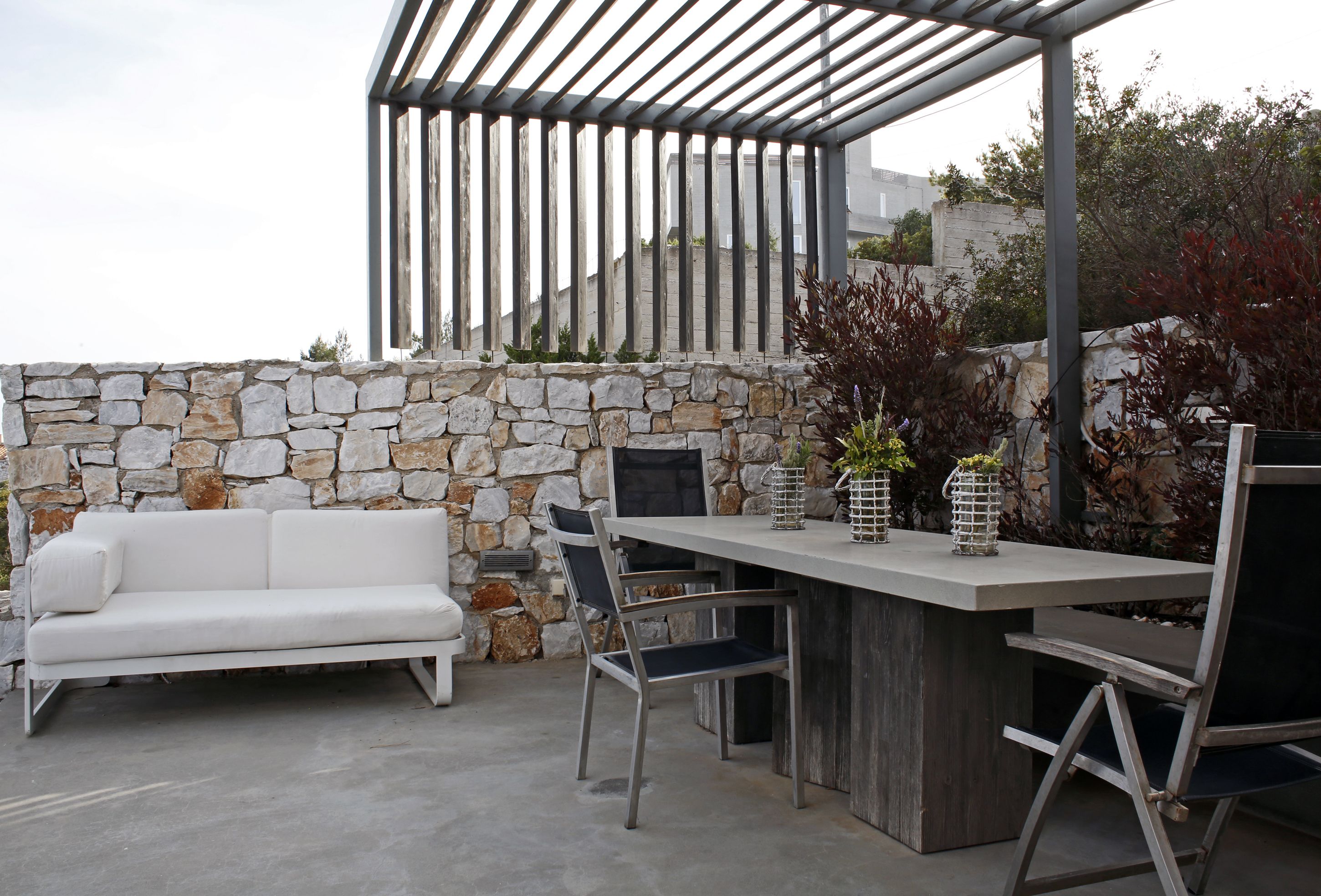 An outdoor patio with a stone wall, a white sofa, and a table with chairs.